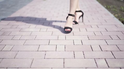 Feet of young woman in high-heeled footwear going in the city .. Female legs in high heels shoes walking in the urban street. Slow motion