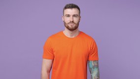 Excited joyful tattooed bearded young man in orange t-shirt isolated on violet background. People lifestyle concept. Tattoo translate life is fight. Pointing on himself put hands on chest ask who me