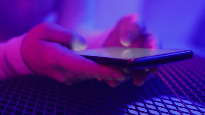 Use of mobile phone in shining neon light indoors. Creative vivid color of ultraviolet red and blue. Hands of person typing and messaging in chat closeup. Trendy neon room and colorful party concept Royalty-Free Stock Footage #1066528105