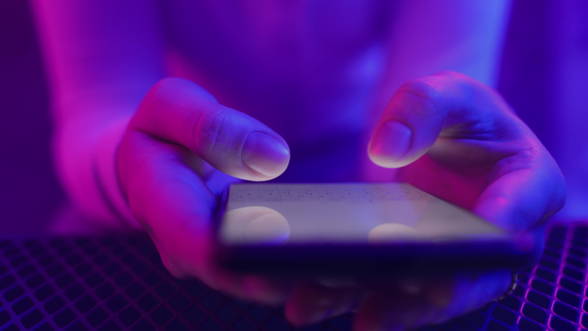 Use of mobile phone in shining neon light indoors. Creative vivid color of ultraviolet red and blue. Hands of person typing and messaging in chat closeup. Trendy neon room and colorful party concept | Shutterstock HD Video #1066528105