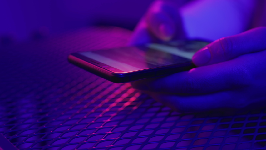 Use of mobile phone in shining neon light. Creative vivid color of ultraviolet red and blue. Hands of person scrolling up photos of instagram. Trendy social media photograph close-up at dark neon room | Shutterstock HD Video #1066528129