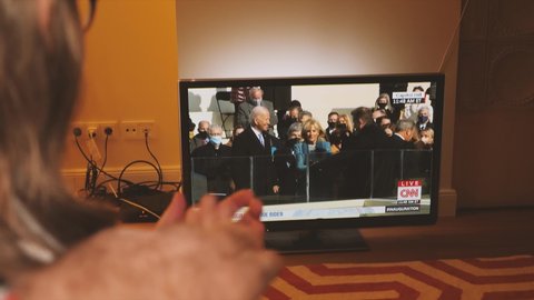 Paris, France - Jan 21, 2021: Couple happy watching TV breaking news of Presidential Inauguration ceremony of Joe Biden the 45th President United States of America and Kamala Harris as vice president