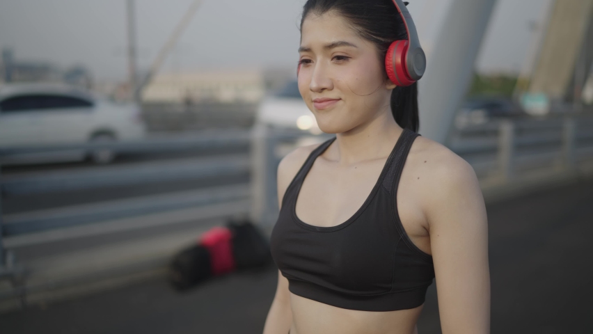 Slow motion video. A white Asian woman wearing a black sports bra. Black trousers And red headphones Viewing an exercise watch On a bridge across the river in the middle of the city
 Royalty-Free Stock Footage #1066531114
