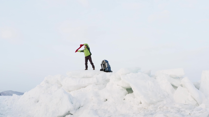 View from below of a happy woman dancing and waving the red scarf on big icy blocks against the blue sky. Winter