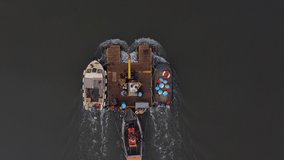 A top down aerial video of a work boat tug pushing a crane barge with other boats being towed.