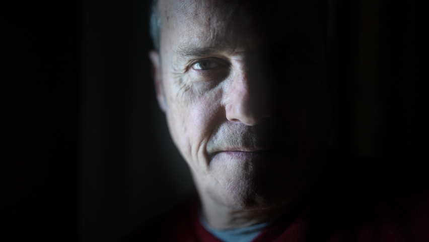 Dramatic portrait of an attractive mature man in a low light who is looking at the camera and smiling. Relieved and hopeful expression. Royalty-Free Stock Footage #1066542472