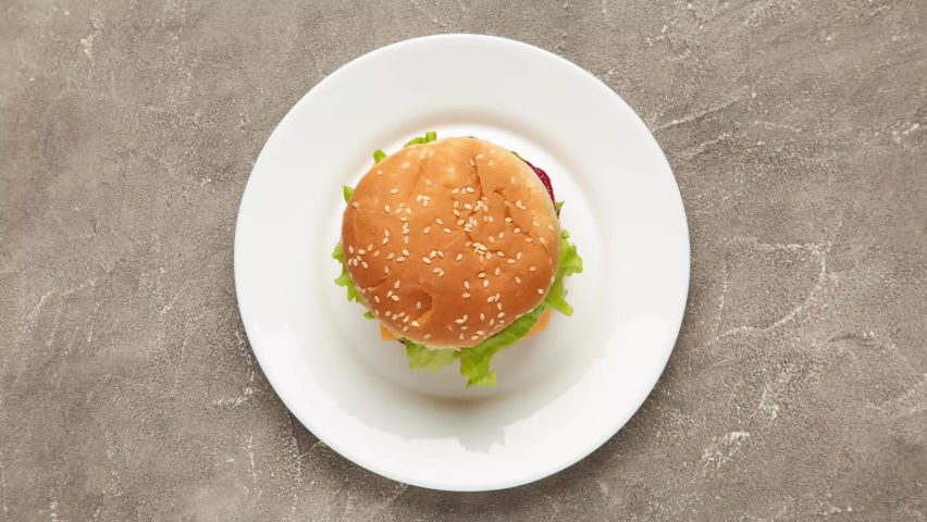 Hamburger on white plate. Delicious burger eating animation, stop motion. Fast food concept
