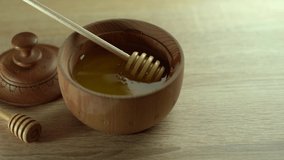 Honey dripping, pouring from honey dipper in wooden bowl. Close-up. Healthy organic Thick honey dipping from the wooden honey spoon, closeup. 4K UHD video footage. Slow motion