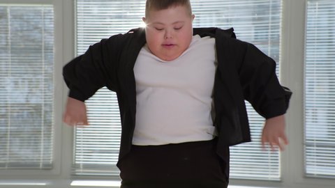 life with disabilities, chubby boy child with down syndrome having fun and jumping on a trampoline on background of window closeup