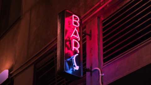 City Nightlife Neon bar sign, alcohol, and cocktails available. Handheld shot. Socializing, alcoholism, dating binge drinking culture. High quality 4k footage.