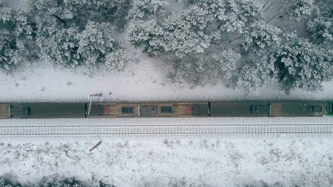 Train passenger transport moving forward on railways in winter snowfall. Train moves trough winter frozen forest on track rails. Train top view winter nature.