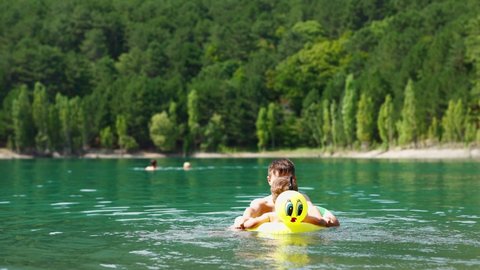 children floating on inflatable circles in mountain lake with clear blue water. two boys brothers swimming, hot summer bathing, enjoing vacation outdoors. Family outdoor adventure