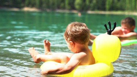 children floating on inflatable circles in mountain lake with clear blue water. two brothers swimming, hot summer bathing, enjoing vacation outdoors. Family outdoor adventure