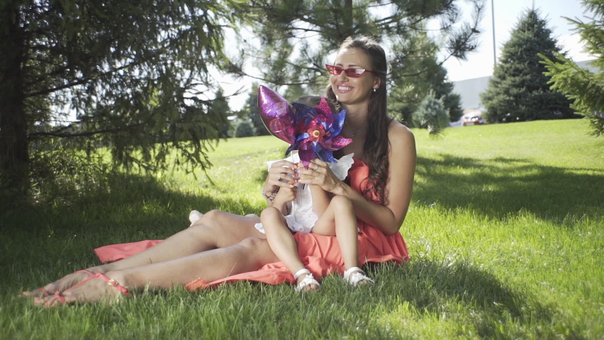 Little beautiful girl with mom on the grass plays with toys in the park