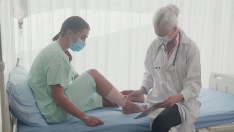 Doctor woman discussing with patient about injured of bone leg and looking tablet on bed at hospital, physician and female talking about accident with foot while bandage at clinic, medical concept.