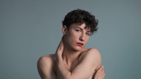 Androgyny. Transgender guy with makeup posing on grey background. Close-up. Masculine and feminine characteristics in one person. Gender identity concept 4k