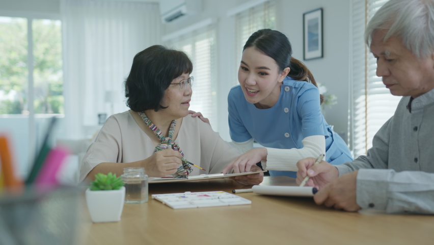 Attractive young senior asian citizen couple sit at home watercolor painting artwork on desk table with nurse feeling happy in mental health therapy or asia older people quarantine activity lifestyle. | Shutterstock HD Video #1066559470
