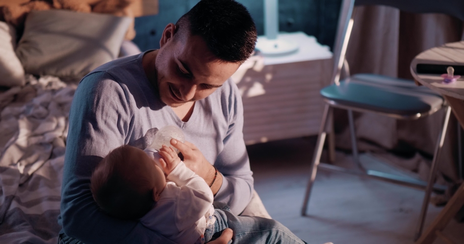 Young dad feeds the newborns, the young man gives the baby a little late in the evening. The male parent feeds the infants.  Royalty-Free Stock Footage #1066564792