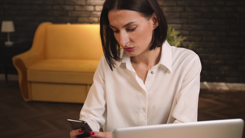  Pretty tired caucasian woman yawning while using phone, communicates, browses, watching content, social networks at home or office..