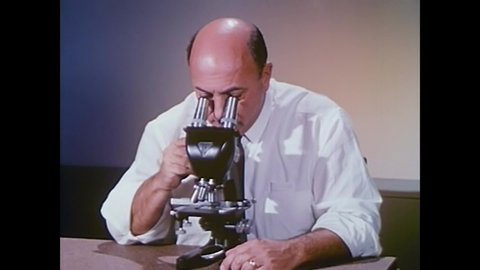 CIRCA 1960s - A perplexed scientist looks through his microscope and sees amoeba seeming to dance to jazz music in 1964.