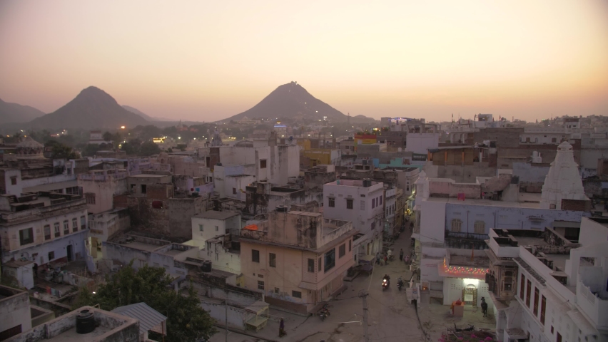 Panorama of Pushkar, Rajasthan, India during sunset with hills in background. Beautiful atmospheric wide shot of the holy Indian city with an orange sky. 4K.