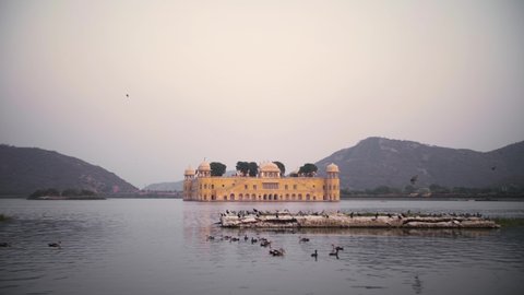 Birds on the lake at the Jal Mahal water palace in Jaipur, Rajasthan, India. Romantic scenery of the famous tourist destination during a beautiful sunset. Slow-motion, 4K.