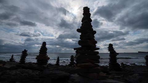Emotional gimbal film timelapse dramatic clouds motion over high stone pyramids, cairn on wild sea ocean beach. Ancient beliefs ritual of folding stones making a wish. Dramatic sky seascape. Sun shine