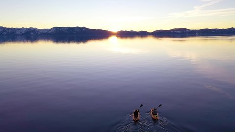 LAKE TAHOE, CALIFORNIA - CIRCA 2020s - Drone aerial at sunset of two kayaks kayakers couple kayaking rowing on the calm waters.