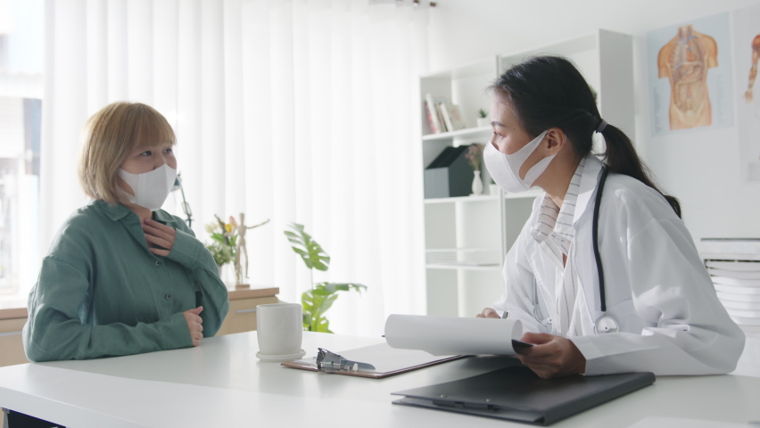 Young Asia lady doctor wear protective mask using clipboard is delivering great news talk discuss results or symptoms with girl patient in hospital office. Lifestyle new normal after corona virus. | Shutterstock HD Video #1066573051