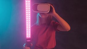 Portrait of a young beautiful girl in virtual reality glasses on a black background. A girl with a virtual sword plays a computer game.
