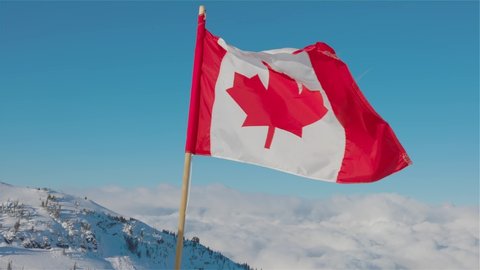 Canadian Flag with a winter mountain landscape in the background. bright and sunny morning. Taken in Whistler, British Columbia, Canada. Slow Motion