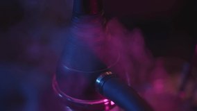 Closeup of black hookah in the bar, neon lights with smoke. Bar pink and blue dark interior with hookah and clouds of smoke on the foreground