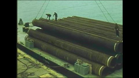 CIRCA 1970s - The pipe sections are loaded from the lighter barges onto trucks at Prudhoe Bay, Alaska.