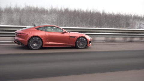 Moscow, Russia - CIRCA 2021: red Jaguar F-type R Coupe driving fast on the highway. Winter forest.