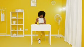 Young stylish African woman is sitting at white desk in creative yellow office space and eating tasty pizza, having lunch, concept of creative video, Slow motion.