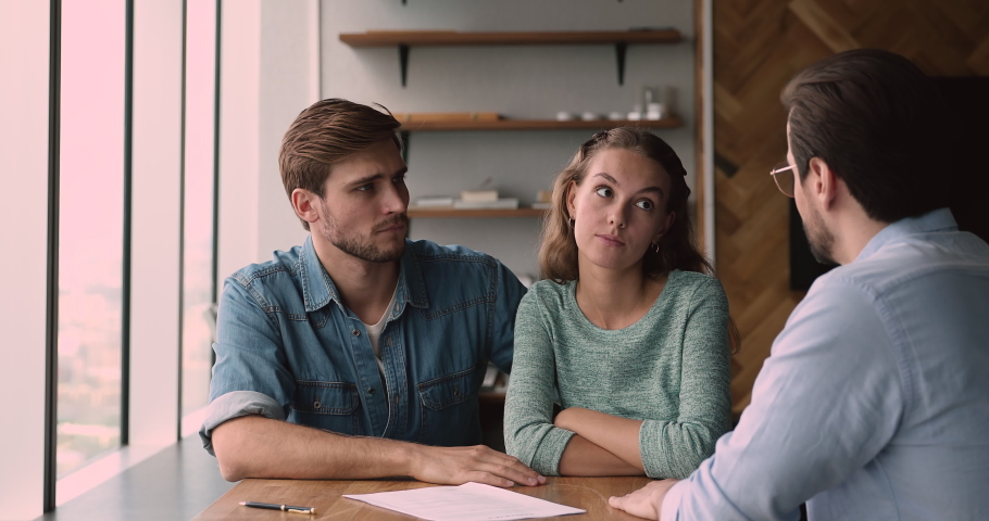 Confused young family couple dissatisfied with contract agreement terms of conditions change, arguing with agent at office meeting. Unhappy clients blaming financial advisor, demanding compensation. Royalty-Free Stock Footage #1066586323