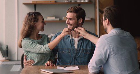 Happy loving family couple discussing apartment purchase with professional real estate agent at office meeting, signing paper contract, getting keys from own accommodation, celebrating successful deal