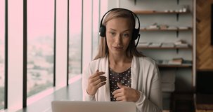 Happy young business woman wearing headphones with microphone, involved in web camera video call meeting with partners, discussing online project. Skilled female teacher giving educational class.