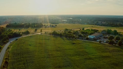 Drone flying above a suburban highway with driving car while sunset.  Aerial view of a suburb road with an automobile. Top view of a roadway in the countryside on the sunset. 
