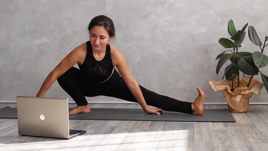 Female doing stretching exercise on yoga mat at home. Sporty woman yoga instructor coaching online, making video of yoga lessons on laptop camera. Attractive fit girl watching yoga lesson in laptop. - Powered by Shutterstock - Get 15% off with code: PIKWIZARD15