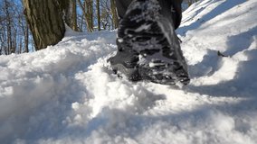 Leg teenager in winter shoes walking on the snow in a winter park.  Sunny winter day outdoor.  Slow motion.