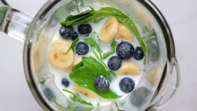Blueberry, banana and spinach smoothie or milkshake blended in blender with splashes. top view. slow motion. Healthy drink concept