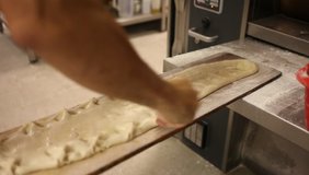 Hands of professional baker preparing traditional Spanish coca for baking, sprinkling dough with pine nuts and sugar and putting into industrial oven. High quality FullHD footage