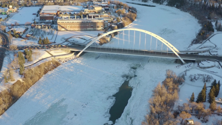 Winter Aerial birds eye view fly over the North Saskatchewan River covered with snow ice and cracked pockets of cold waters headed towards the white modern walter dale bridge on a sunny afternoon 4-5