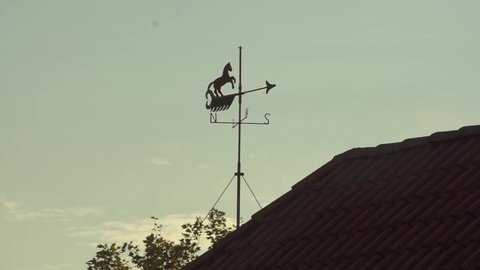 Old weather vane with horse on farm roof after sunrise