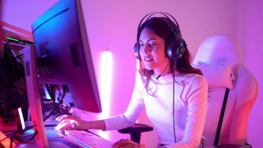 Happy pretty long-haired Asian transgender professional gamer wearing a gaming headset having fun playing online video games on a personal computer in room and raising fist up after winning the game. Royalty-Free Stock Footage #1066606120