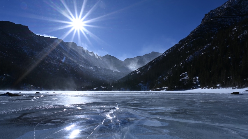 Gusty winds blow snow across an iced over Mills Lake on a bright sunny day in Rocky Mountain National Park, Colorado, USA. 