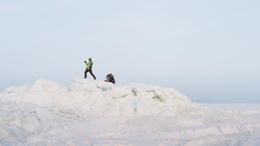 Zooming in aerial view of a happy woman dancing and waving the red scarf on big icy blocks against the blue sky. Seaside. Frozen sea is on the background. Winter