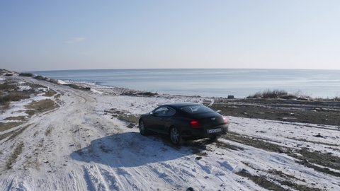 VLADIVOSTOK, RUSSIA - JANUARY 17, 2021: Aerial view of stylish Bentley car on the winter beach to enjoy the view of the sea under the bright sun