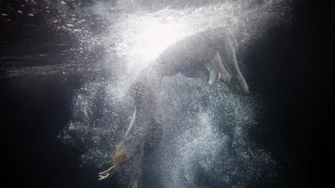 young woman is plunging inside water, underwater shot, slow motion, silhouette of body